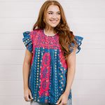 Women wearing a navy top with colorful patter, pink embroidery and ruffle sleeves  showing the front on a white background 