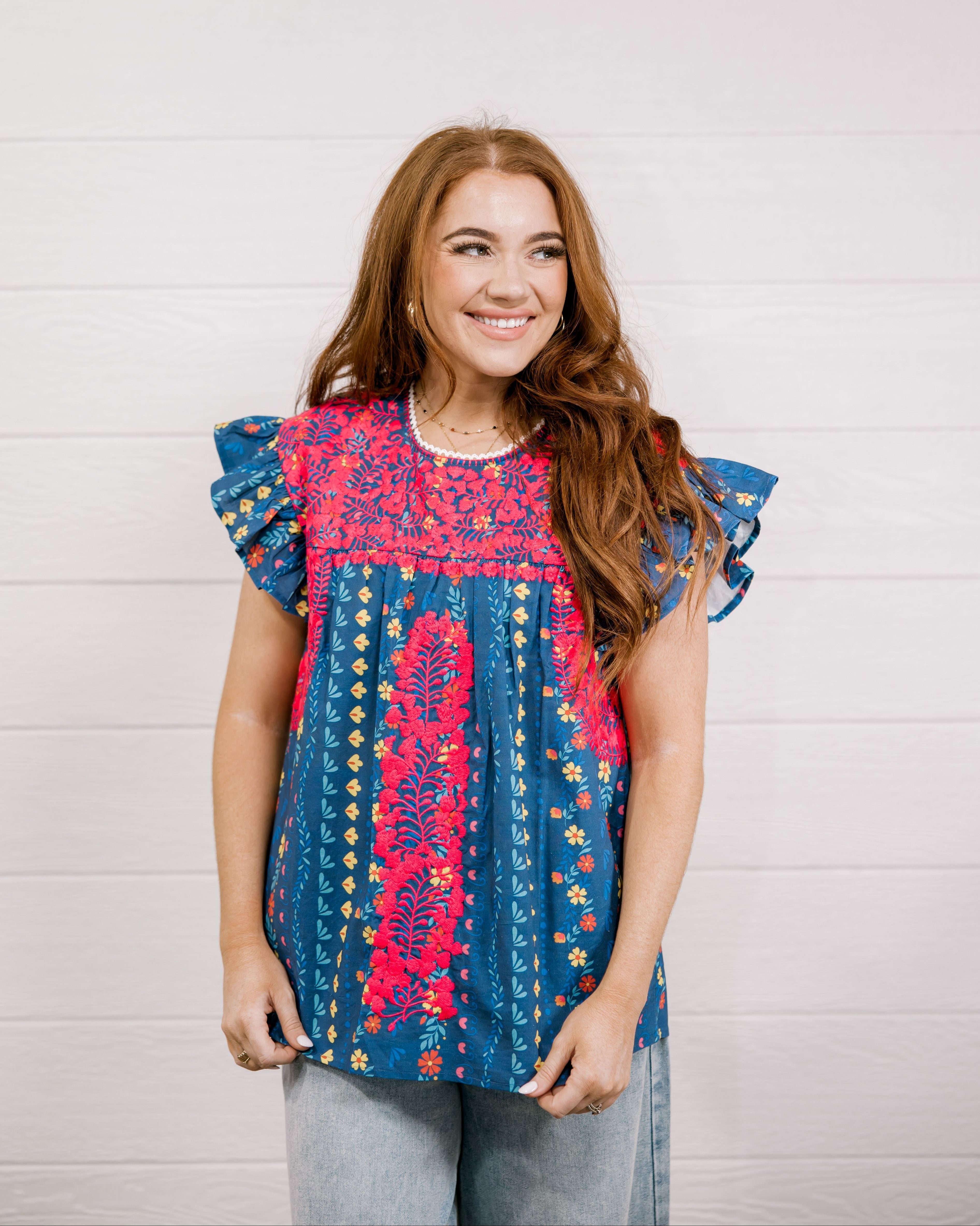 Women wearing a navy top with colorful patter, pink embroidery and ruffle sleeves  showing the front on a white background 