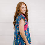 Women wearing a navy top with colorful patter, pink embroidery and ruffle sleeves  showing the side on a white background 