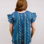 Women wearing a navy top with colorful patter, pink embroidery and ruffle sleeves  showing the back on a white background 