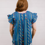 Women wearing a navy top with colorful patter, pink embroidery and ruffle sleeves  showing the back on a white background 