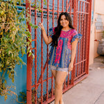 Women wearing a navy top with colorful patter, pink embroidery and ruffle sleeves in a colorful outdoor enviornment 