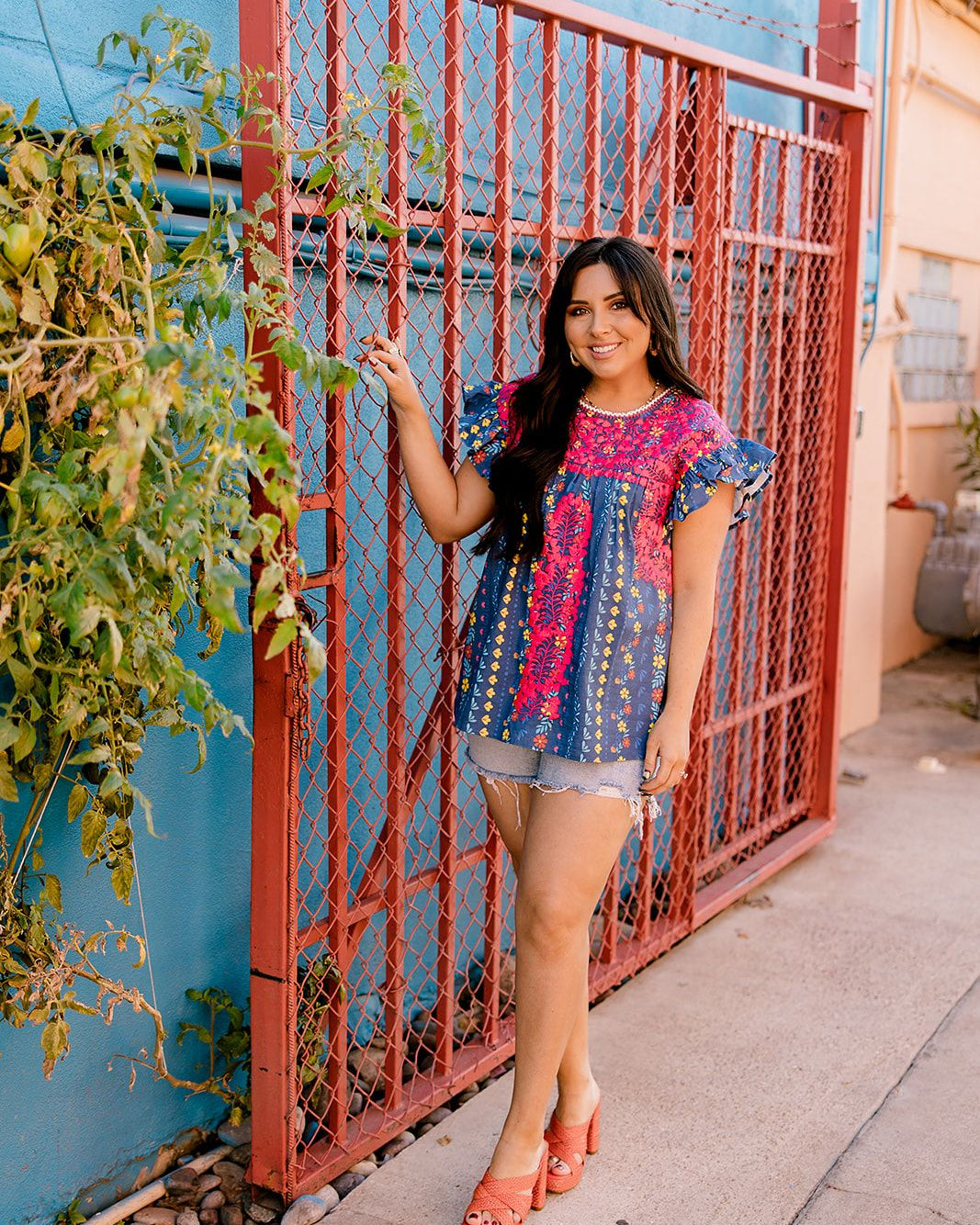 Women wearing a navy top with colorful patter, pink embroidery and ruffle sleeves in a colorful outdoor enviornment 