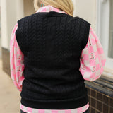 Woman with blonde hair standing in a back profile position wearing the Kodi Vest in a lifestyle scene. The focal point of this image is the cable knit pattern on back of sweater. The model paired this with dark-wash denim jeans and the Jesse Top.