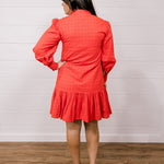 Back view woman wearing a red eyelet dress standing against a white wall.