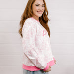 Side view of woman wearing a pink and white patterned sweatshirt with 'LOVED' embroidered in pink standing against a white background.