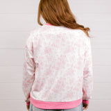 Back view of woman wearing a pink and white patterned sweatshirt with 'LOVED' embroidered in pink standing against a white background.