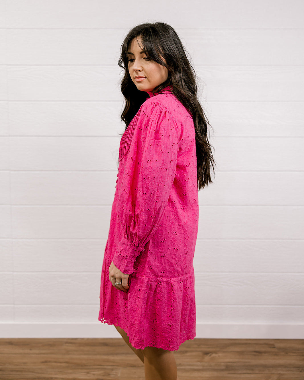 Woman wearing a bright eyelet pink dress against a white wall.