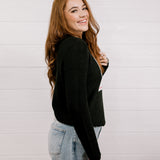 Side view of woman wearing a black sweater with a playing card graphic design featuring a red cowgirl and sequin hearts against a white background. 