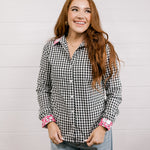 Woman wearing a black and white checkered shirt with pink & white embroidery at collar and wrists against a white background.
