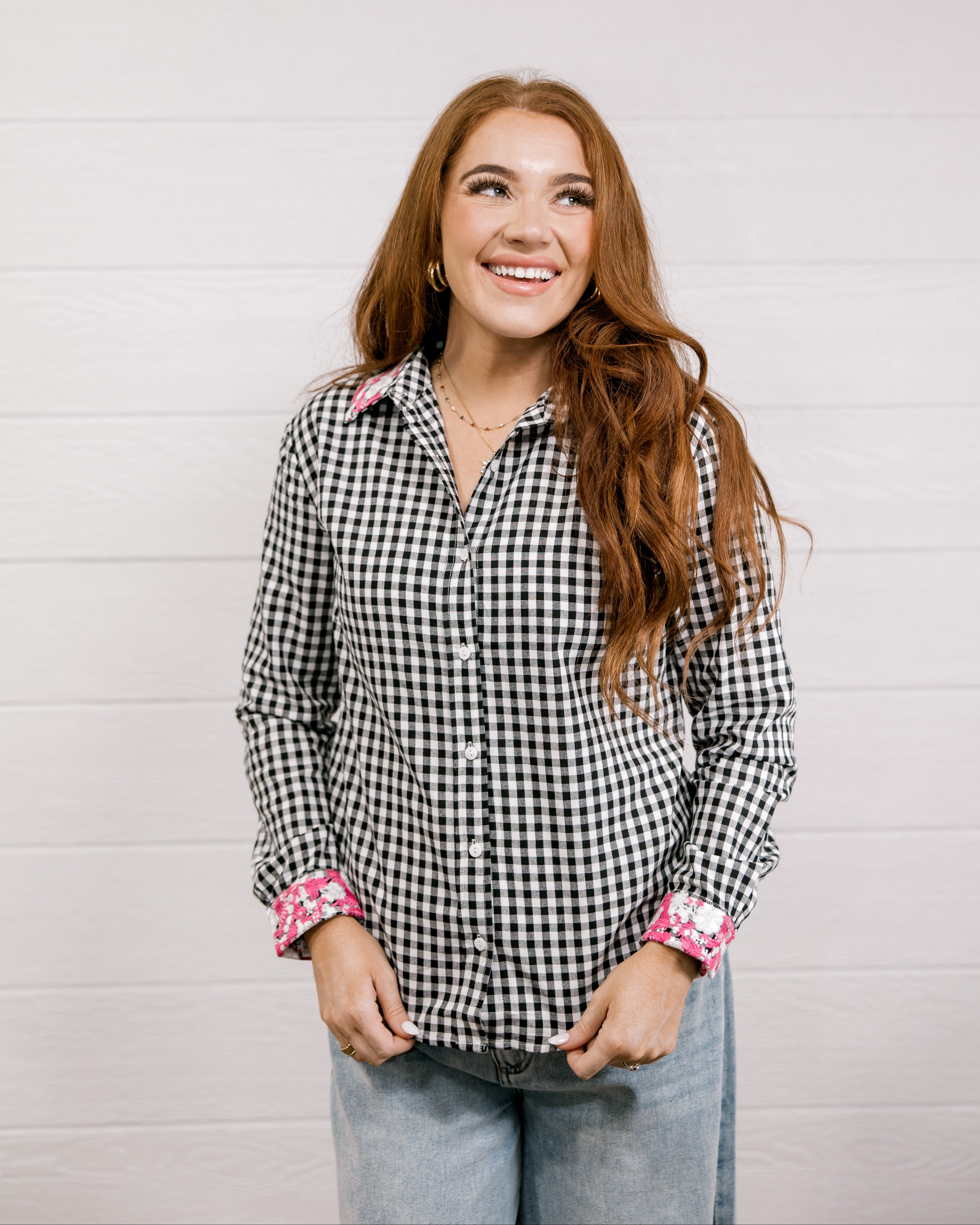 Woman wearing a black and white checkered shirt with pink & white embroidery at collar and wrists against a white background.