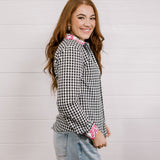 Side view of woman wearing a black and white checkered shirt with pink & white embroidery at collar and wrists against a white background.