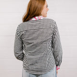 Back view of woman wearing a black and white checkered shirt with pink & white embroidery at collar and wrists against a white background.