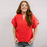 Woman wearing a red textured top with embroidery on puff sleeves against a white background.