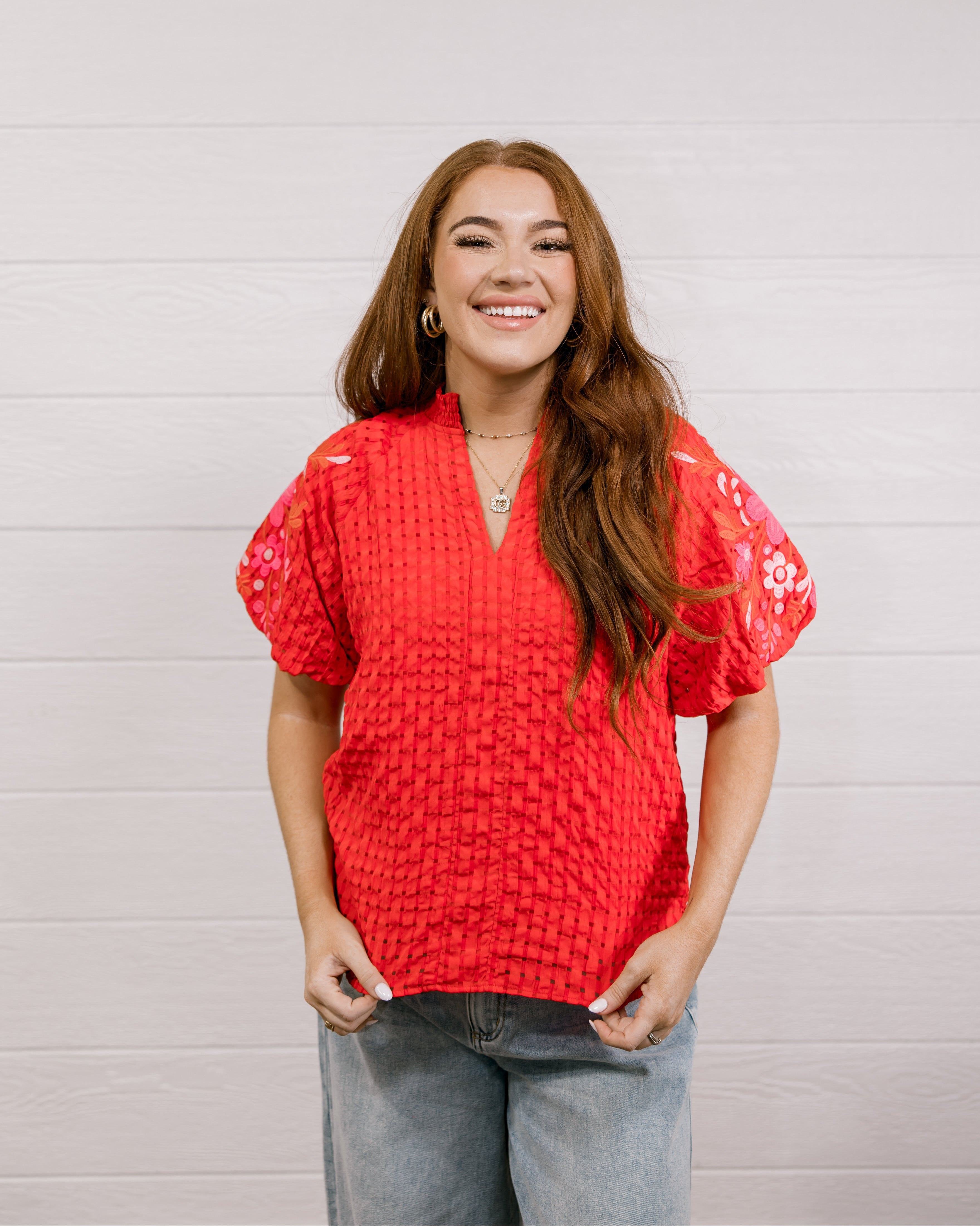 Woman wearing a red textured top with embroidery on puff sleeves against a white background.
