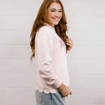 Side view of woman wearing a pink sweatshirt with 'XOXO' embroidered design with scalloped hemline against a white background.