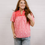 Woman wearing a red patterned blouse that is short sleeve & features red embroidery on front and back against a white background.