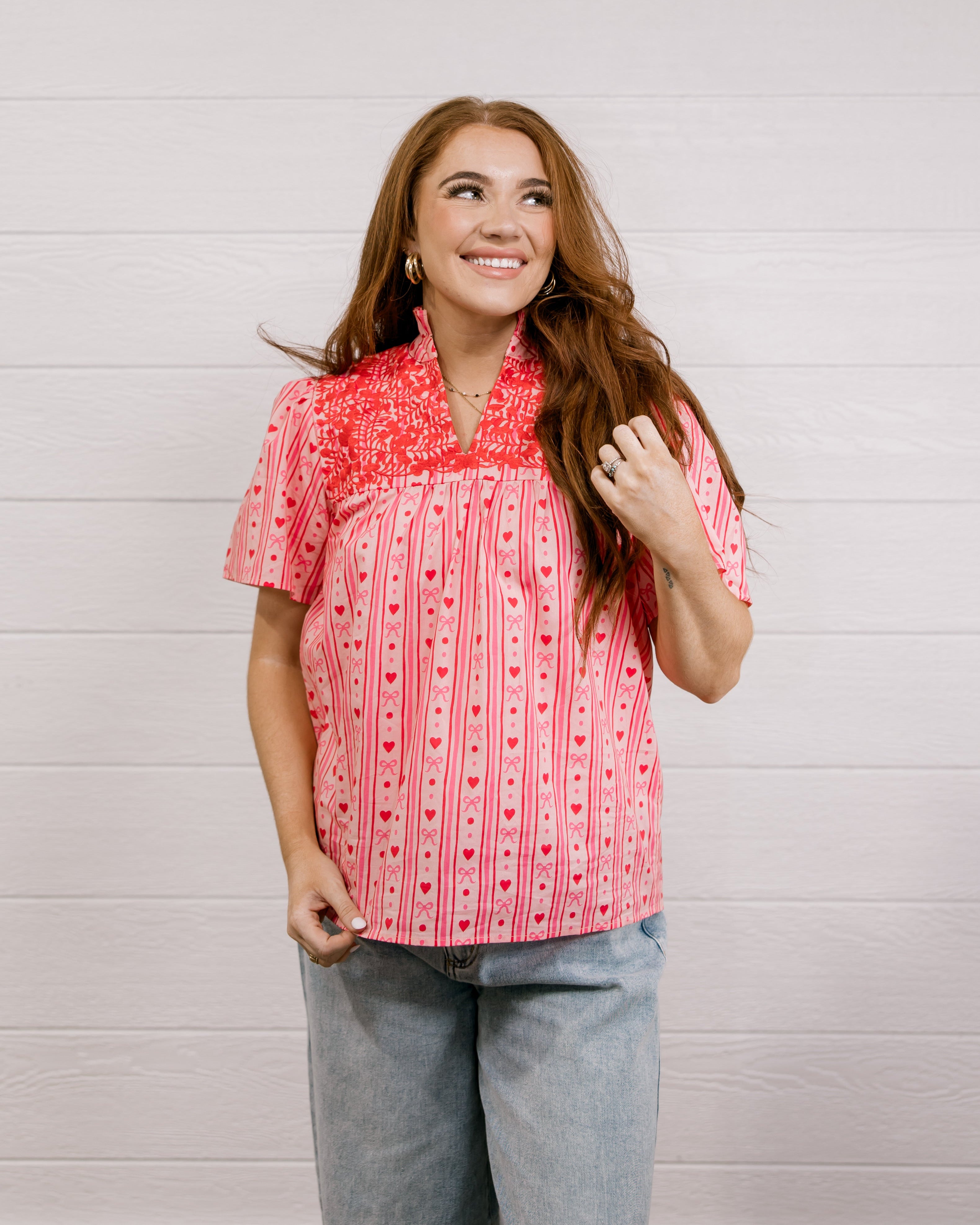 Woman wearing a red patterned blouse that is short sleeve & features red embroidery on front and back against a white background.