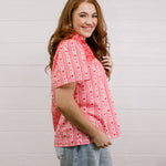 Side view of woman wearing a red patterned blouse that is short sleeve & features red embroidery on front and back against a white background.
