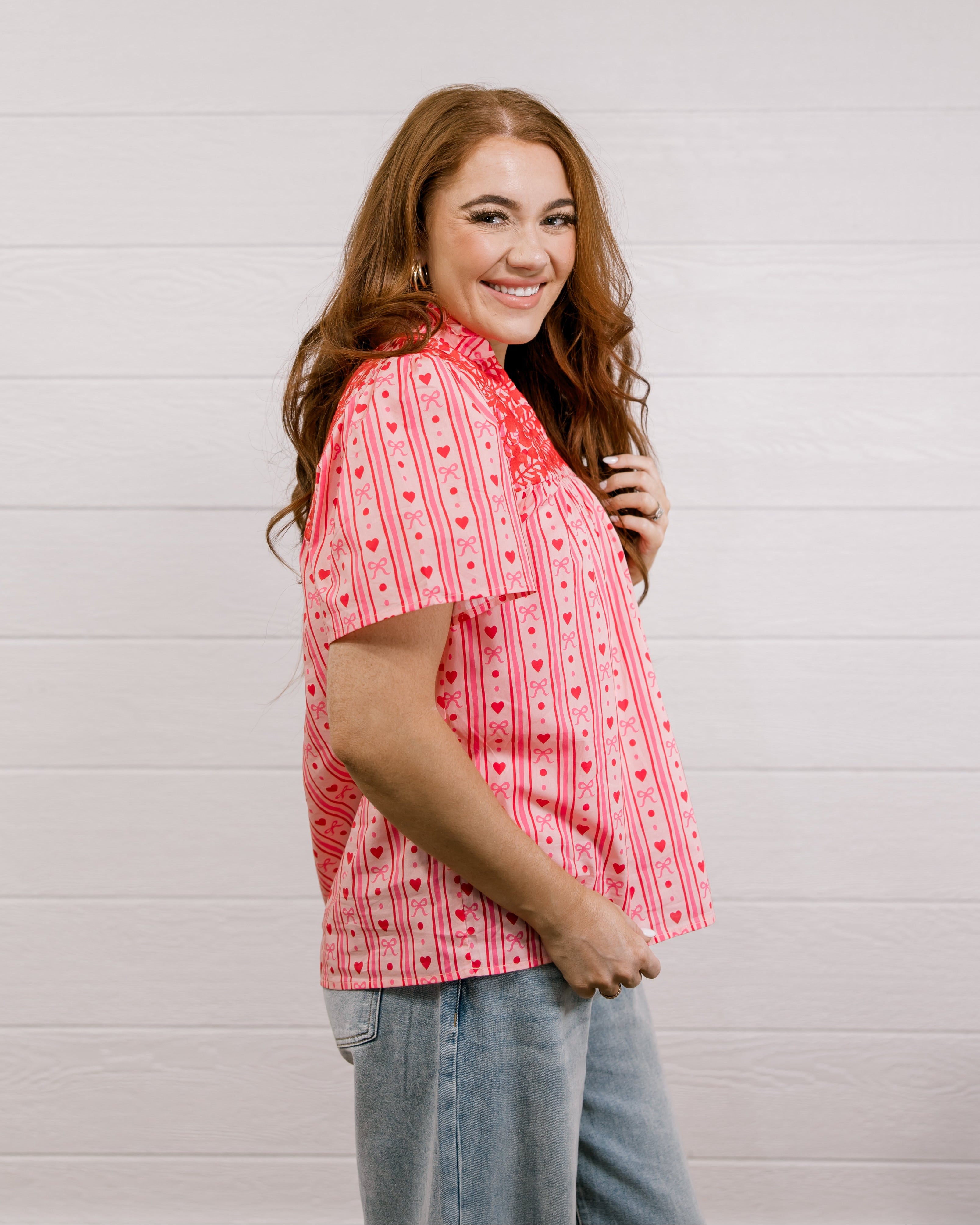 Side view of woman wearing a red patterned blouse that is short sleeve & features red embroidery on front and back against a white background.