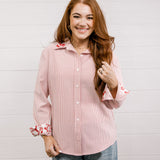 Woman wearing a red blouse that features red & white embroidery on collar & cuff with rolled-up sleeves against a white wall