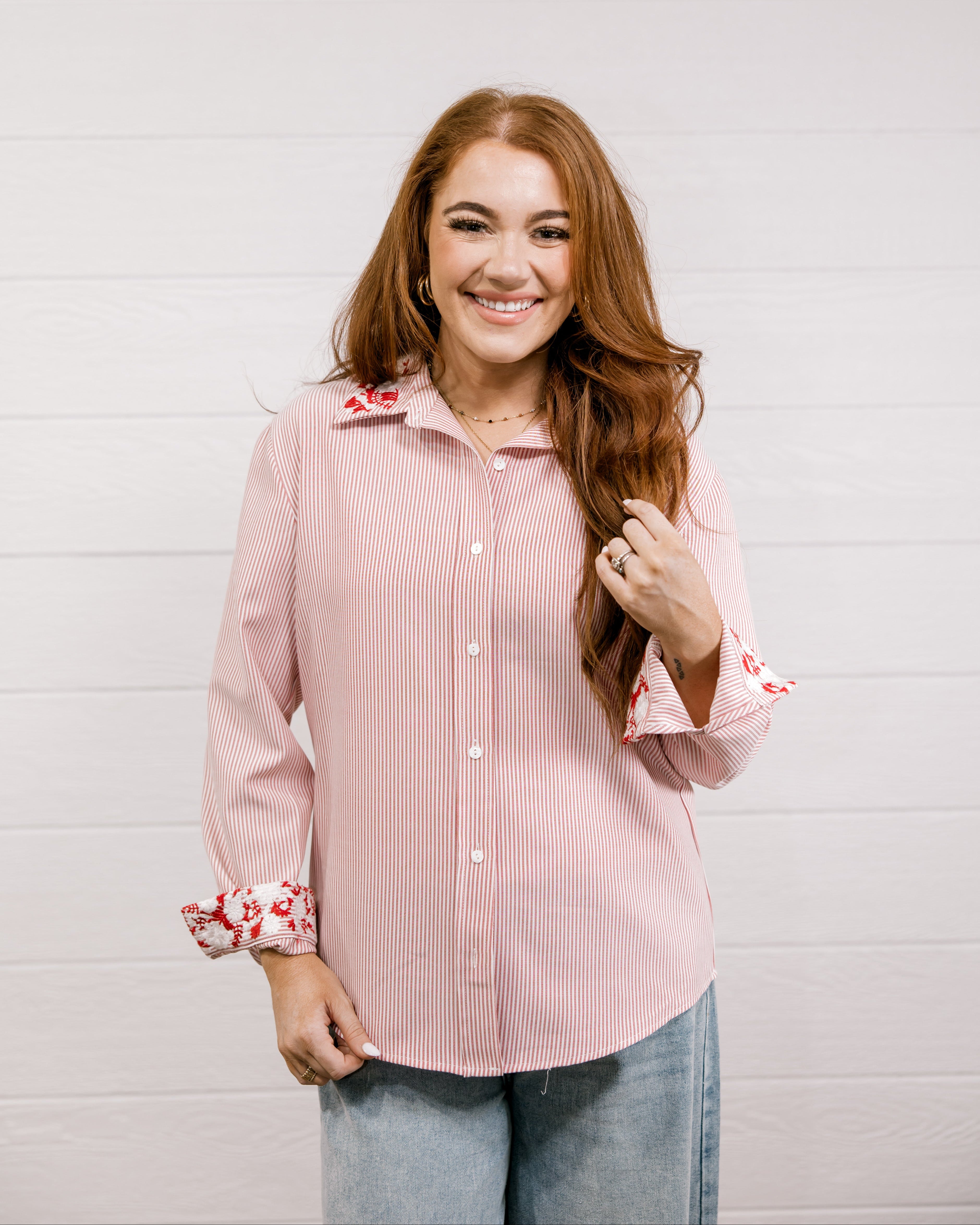 Woman wearing a red blouse that features red & white embroidery on collar & cuff with rolled-up sleeves against a white wall
