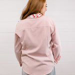 Back view of woman wearing a red blouse that features red & white embroidery on collar & cuff with rolled-up sleeves against a white wall