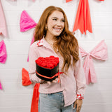 Woman holding a heart-shaped cake against a wall with pink and red bows.