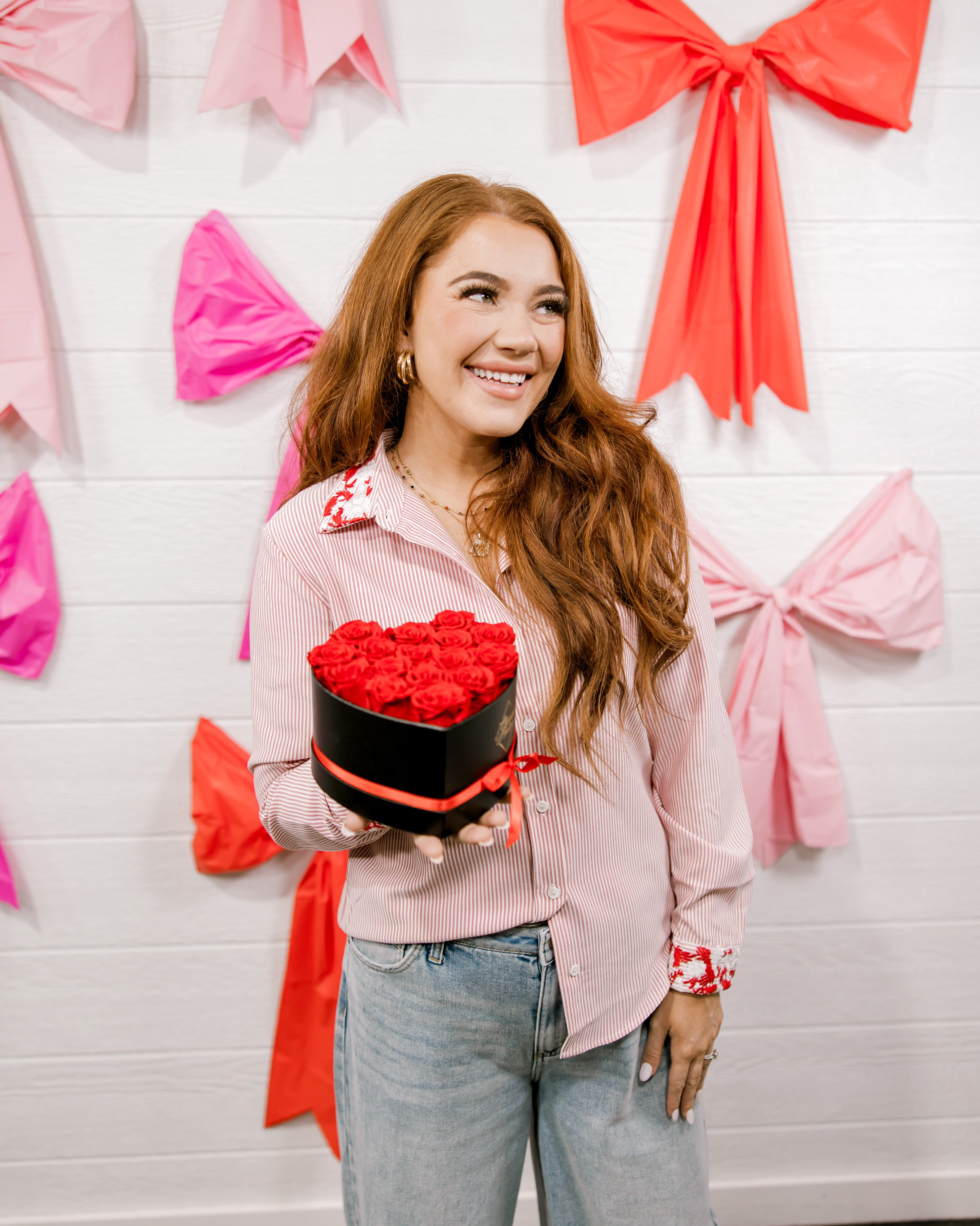 Woman holding a heart-shaped cake against a wall with pink and red bows.