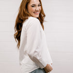 Woman wearing a white blouse and jeans against a plain background