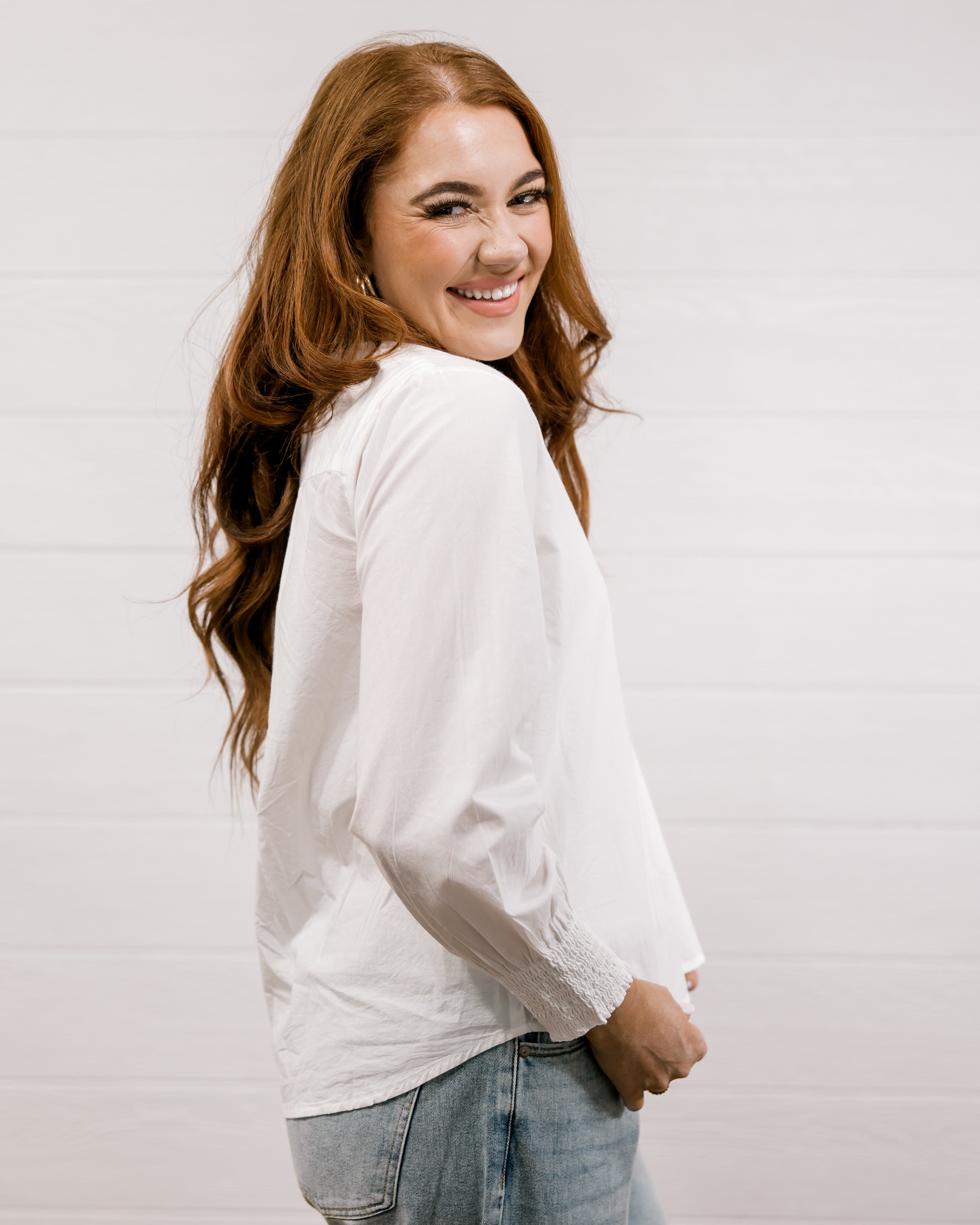 Woman wearing a white blouse and jeans against a plain background