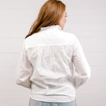 Woman wearing a white blouse with a ruffled collar against a plain background