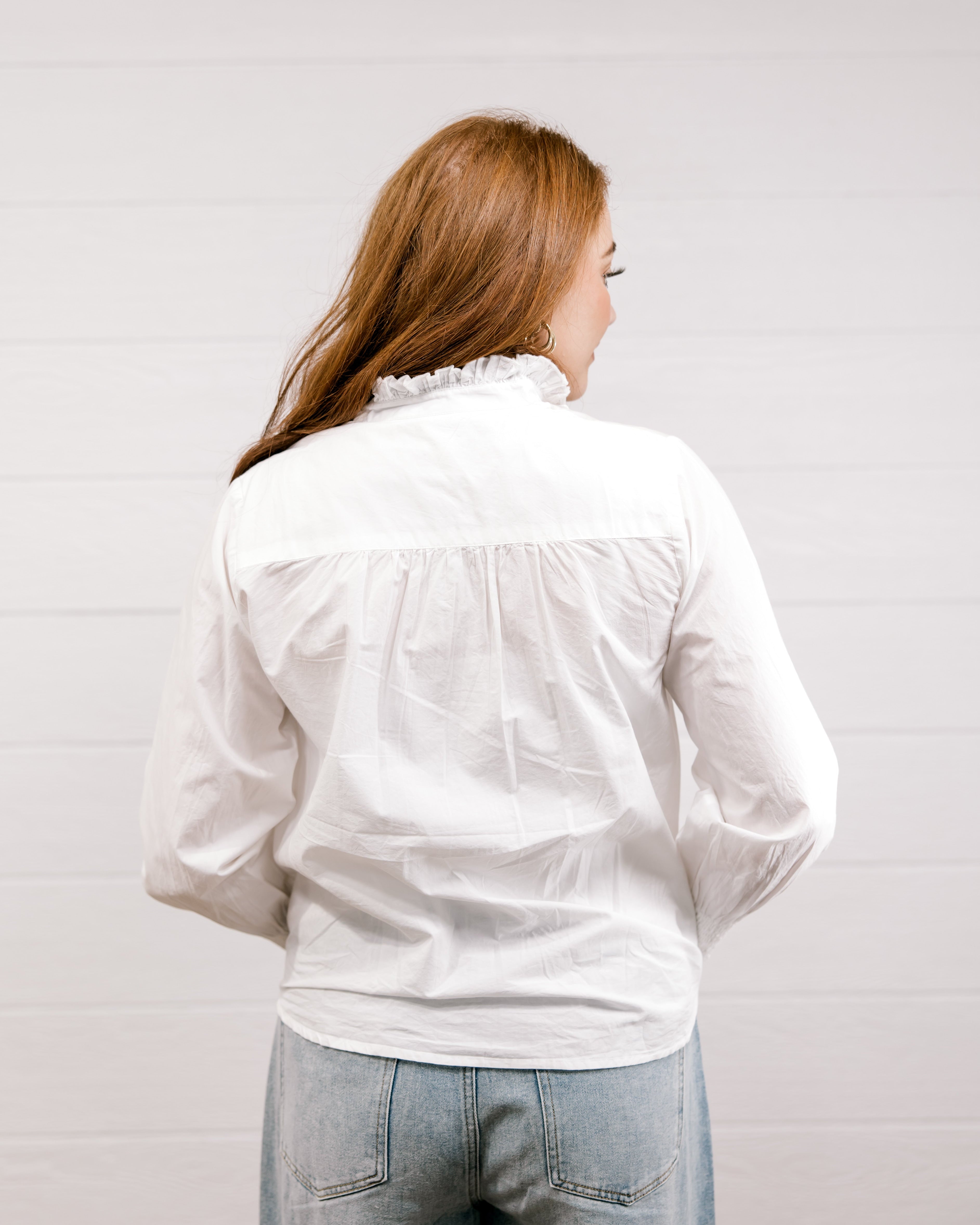 Woman wearing a white blouse with a ruffled collar against a plain background