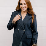 Women wearing a denim blazer with leopard lining in front of a white wall.