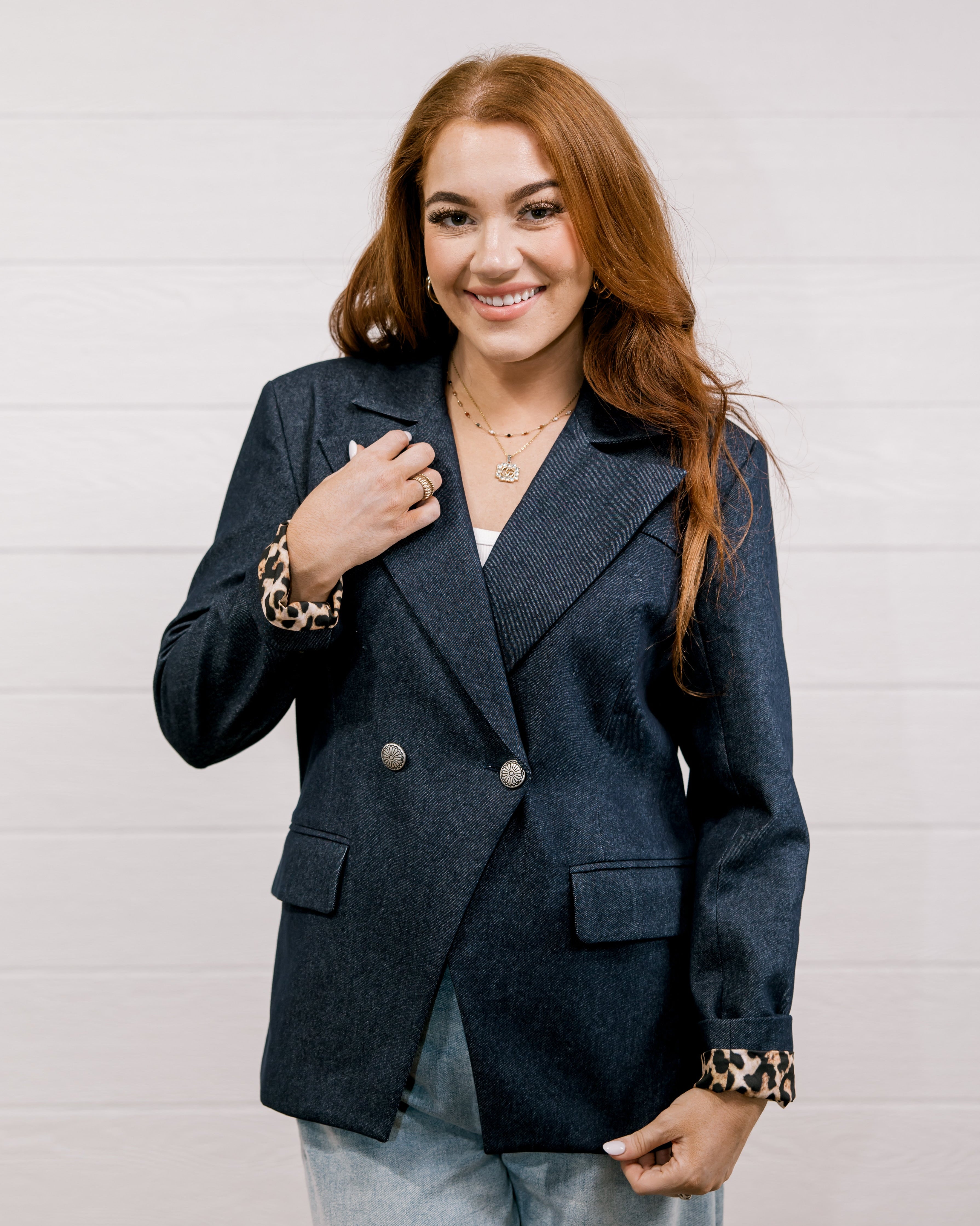 Women wearing a denim blazer with leopard lining in front of a white wall.