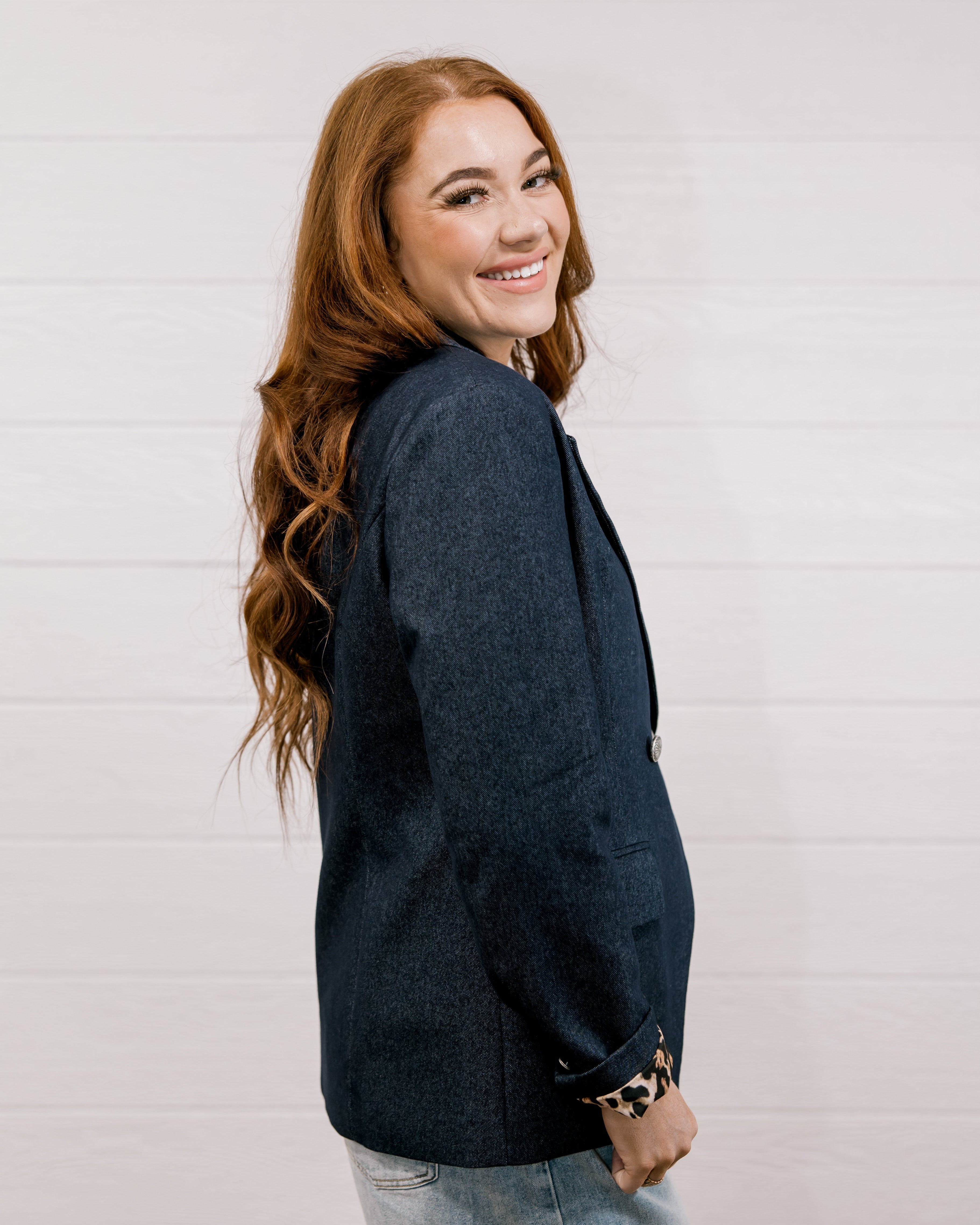 Side view women wearing a denim blazer with leopard lining in front of a white wall.