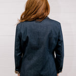 Back view women wearing a denim blazer with leopard lining in front of a white wall.