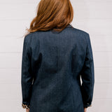 Back view women wearing a denim blazer with leopard lining in front of a white wall.