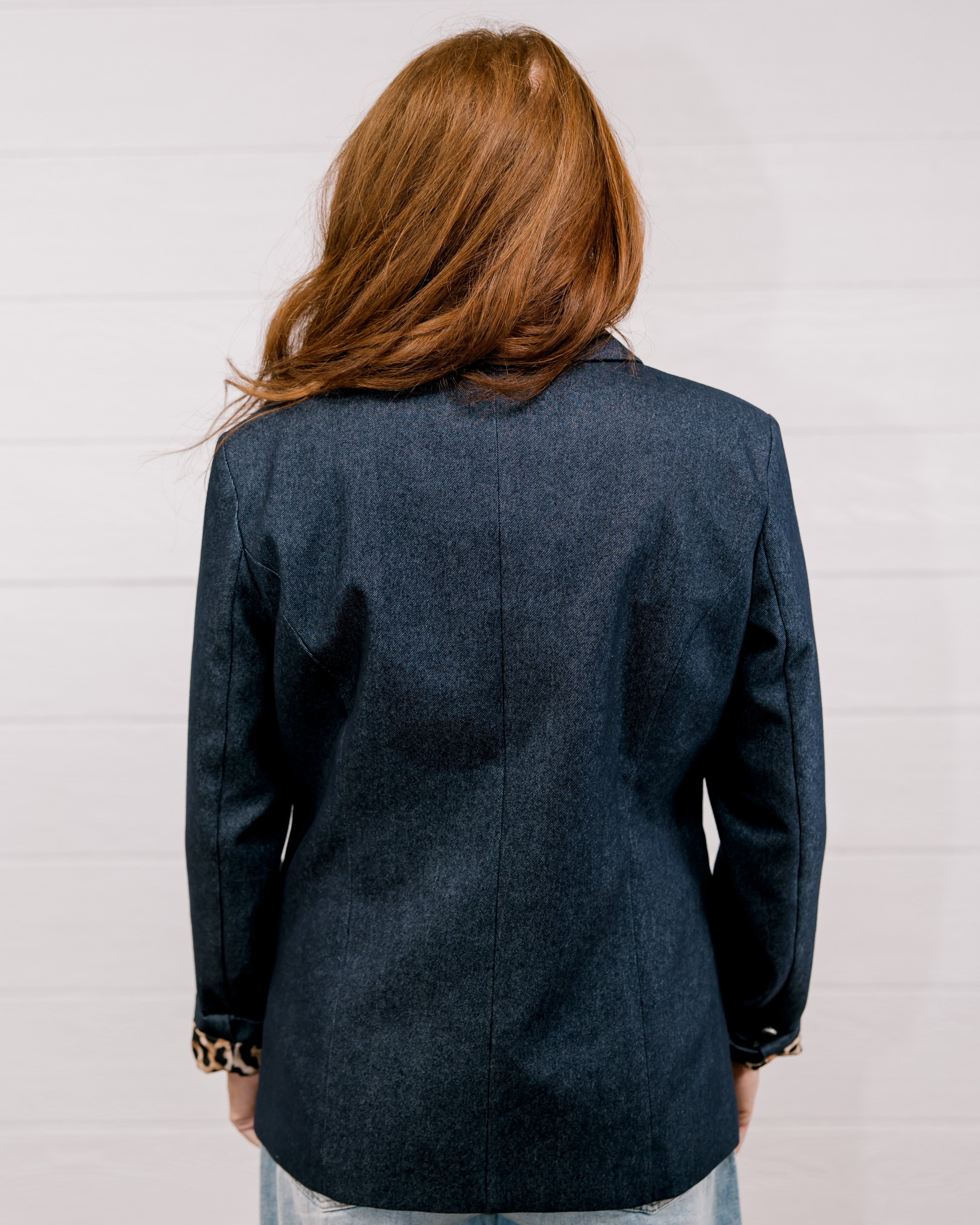 Back view women wearing a denim blazer with leopard lining in front of a white wall.