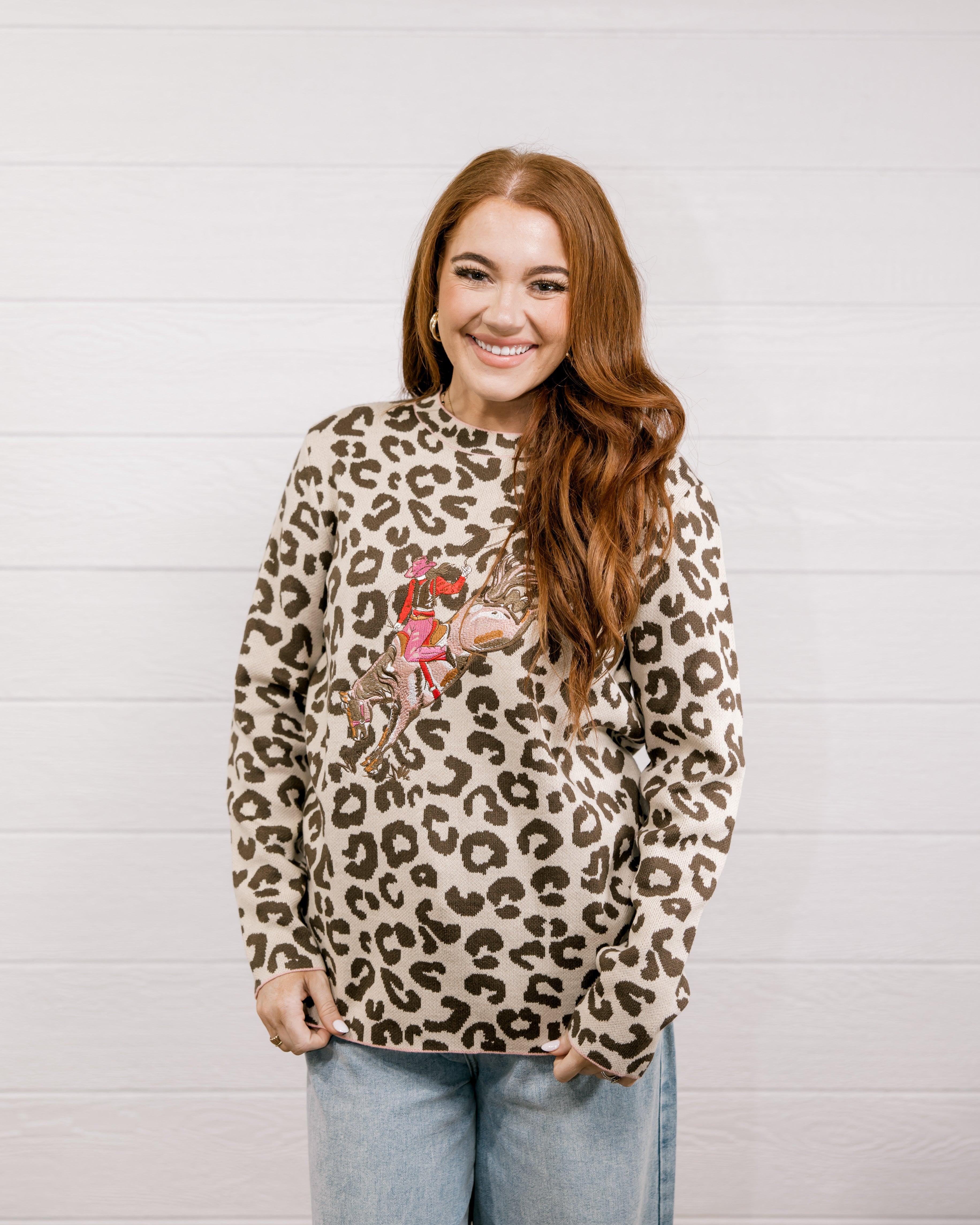 Woman wearing a leopard print sweater with a graphic design against a light wooden panel background