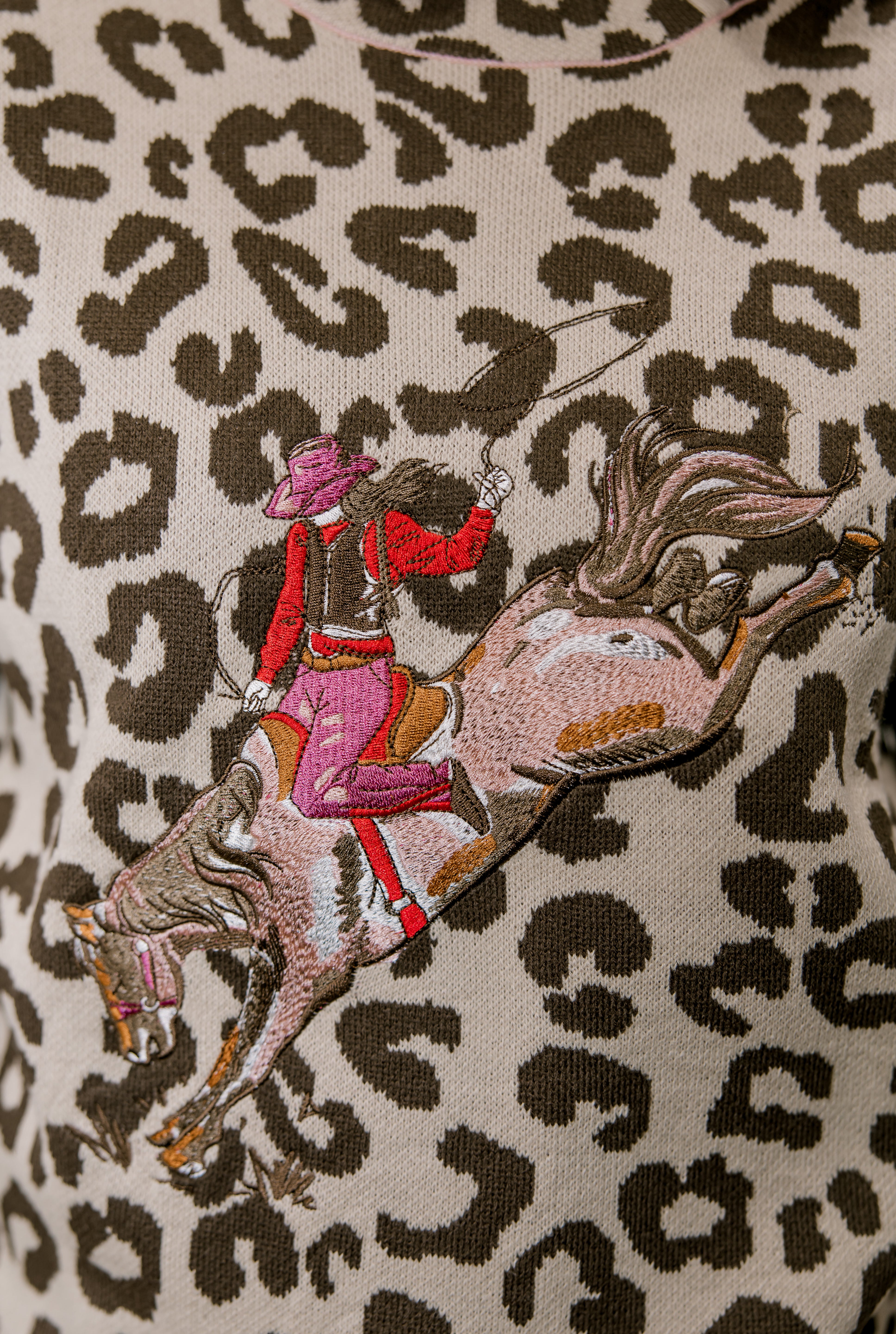 Embroidered design of a person riding a horse on a leopard print background
