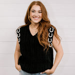 Women wearing a black sweater vest with horse shoes against a white wall.