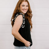 Side view Women wearing a black sweater vest with horse shoes against a white wall.