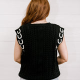 Back view Women wearing a black sweater vest with horse shoes against a white wall.