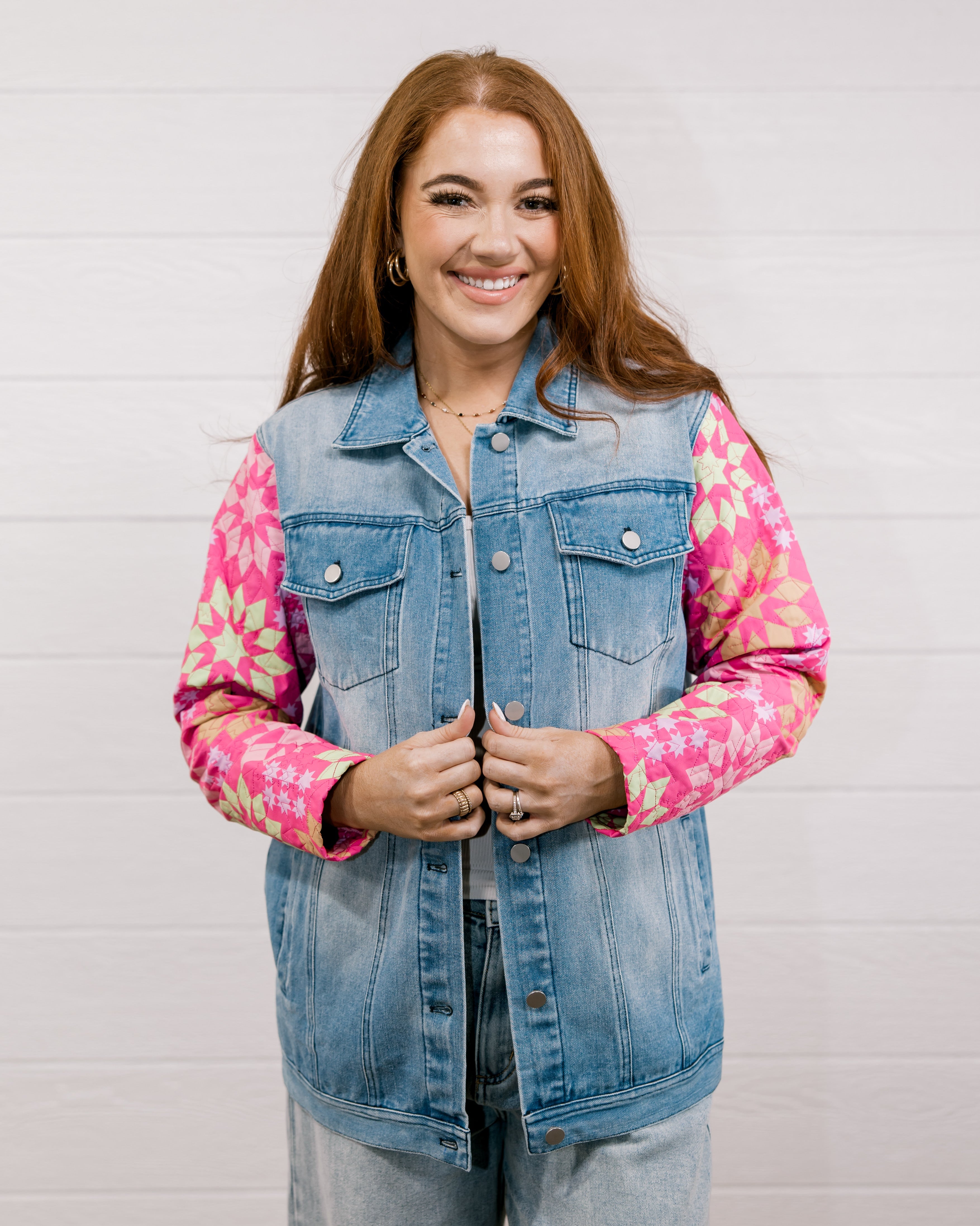 Woman wearing a denim jacket with colorful quilted patchwork sleeves against a white background