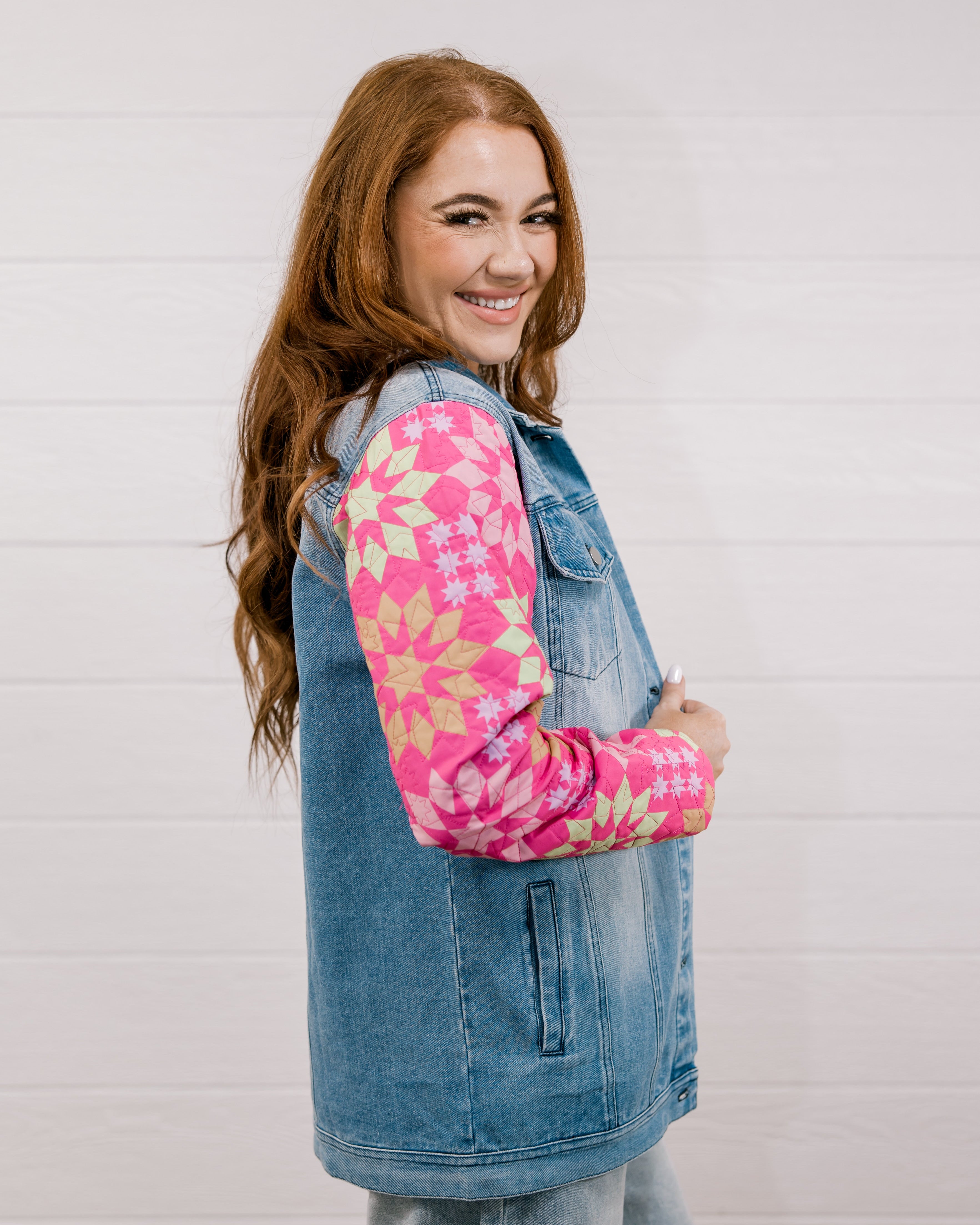 Side view of woman wearing a denim jacket with colorful quilted patchwork sleeves against a white background