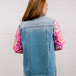 Back view of woman wearing a denim jacket with colorful quilted patchwork sleeves against a white background
