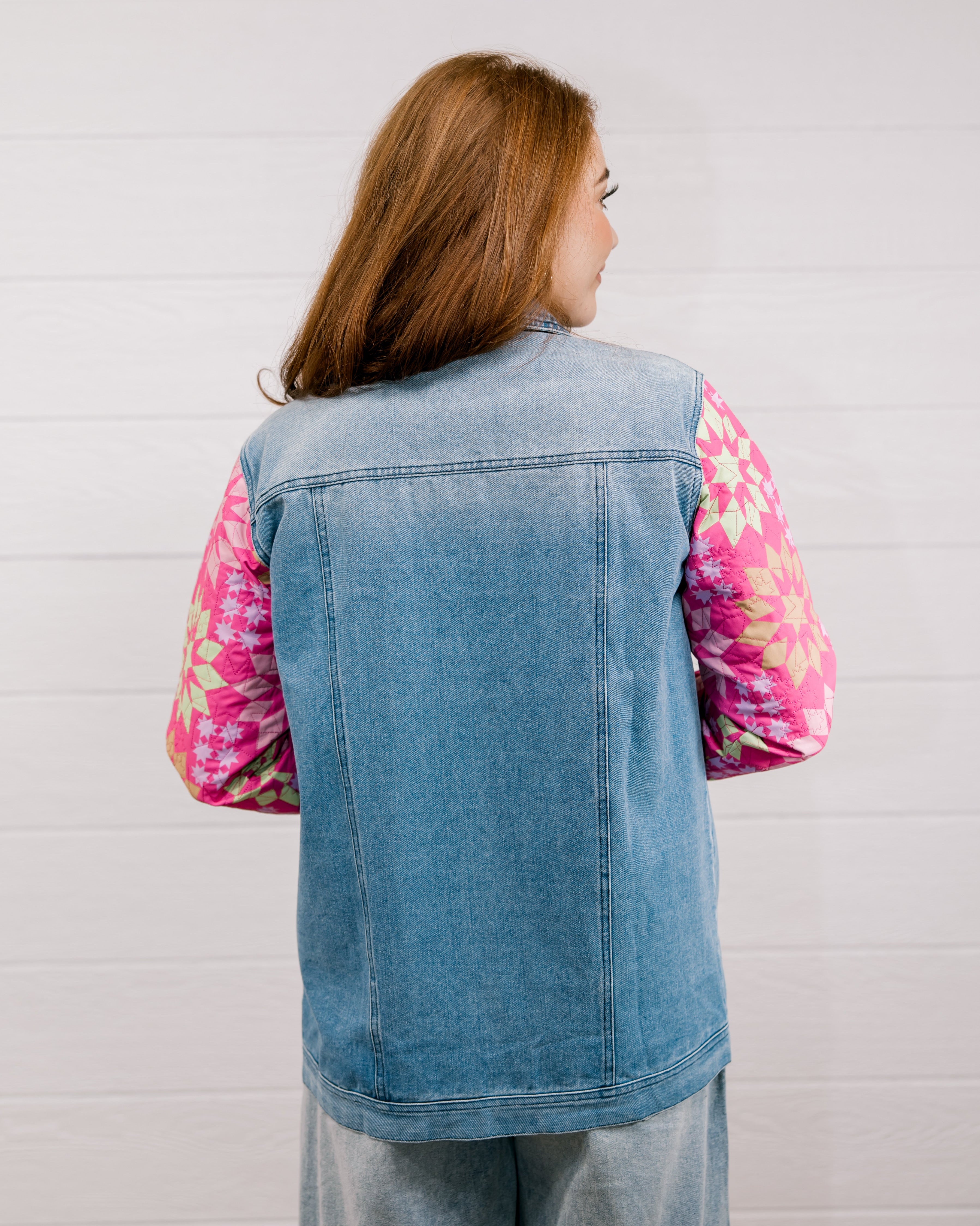Back view of woman wearing a denim jacket with colorful quilted patchwork sleeves against a white background