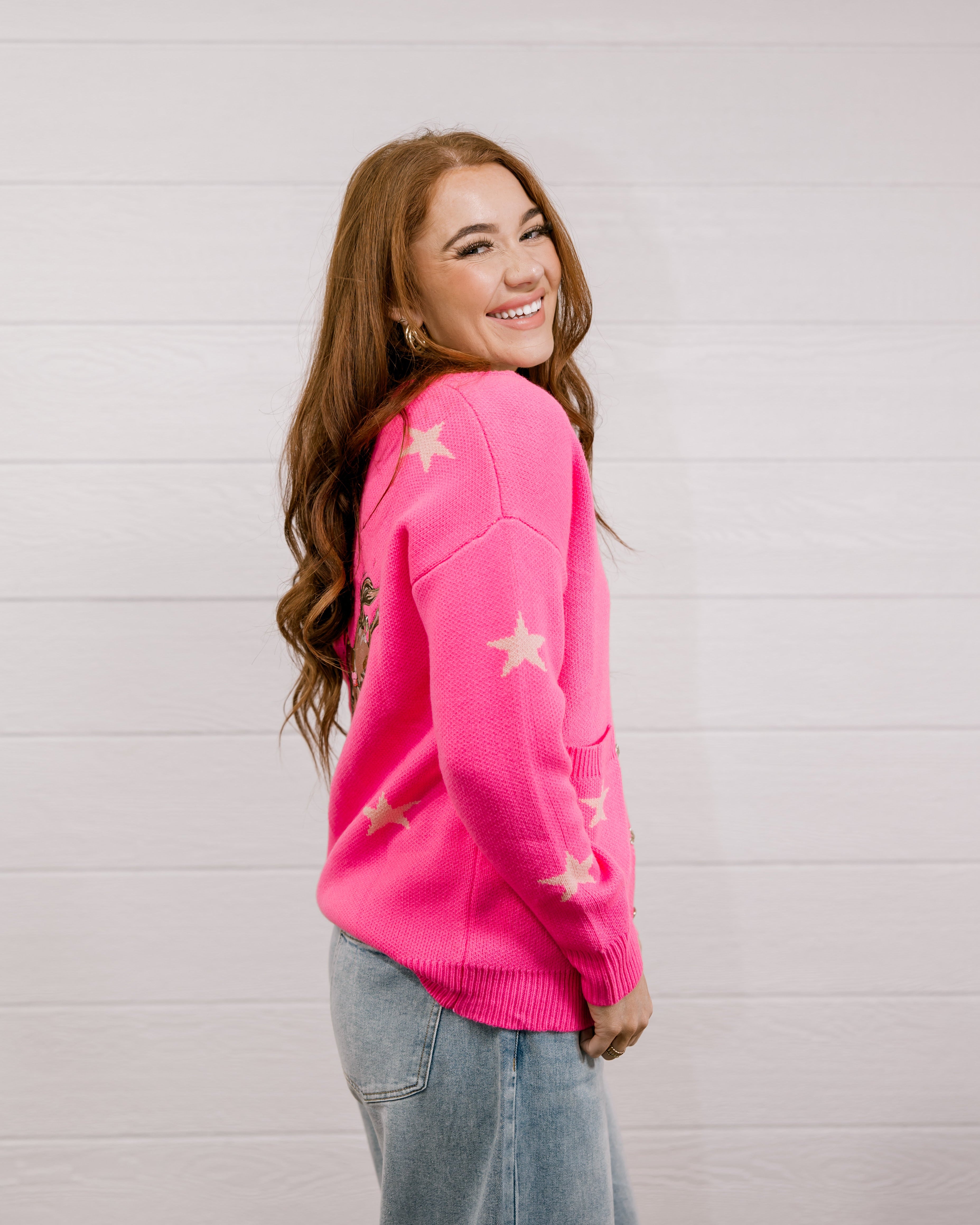 Side view of Woman wearing a bright pink cardigan with star patterns against a white background