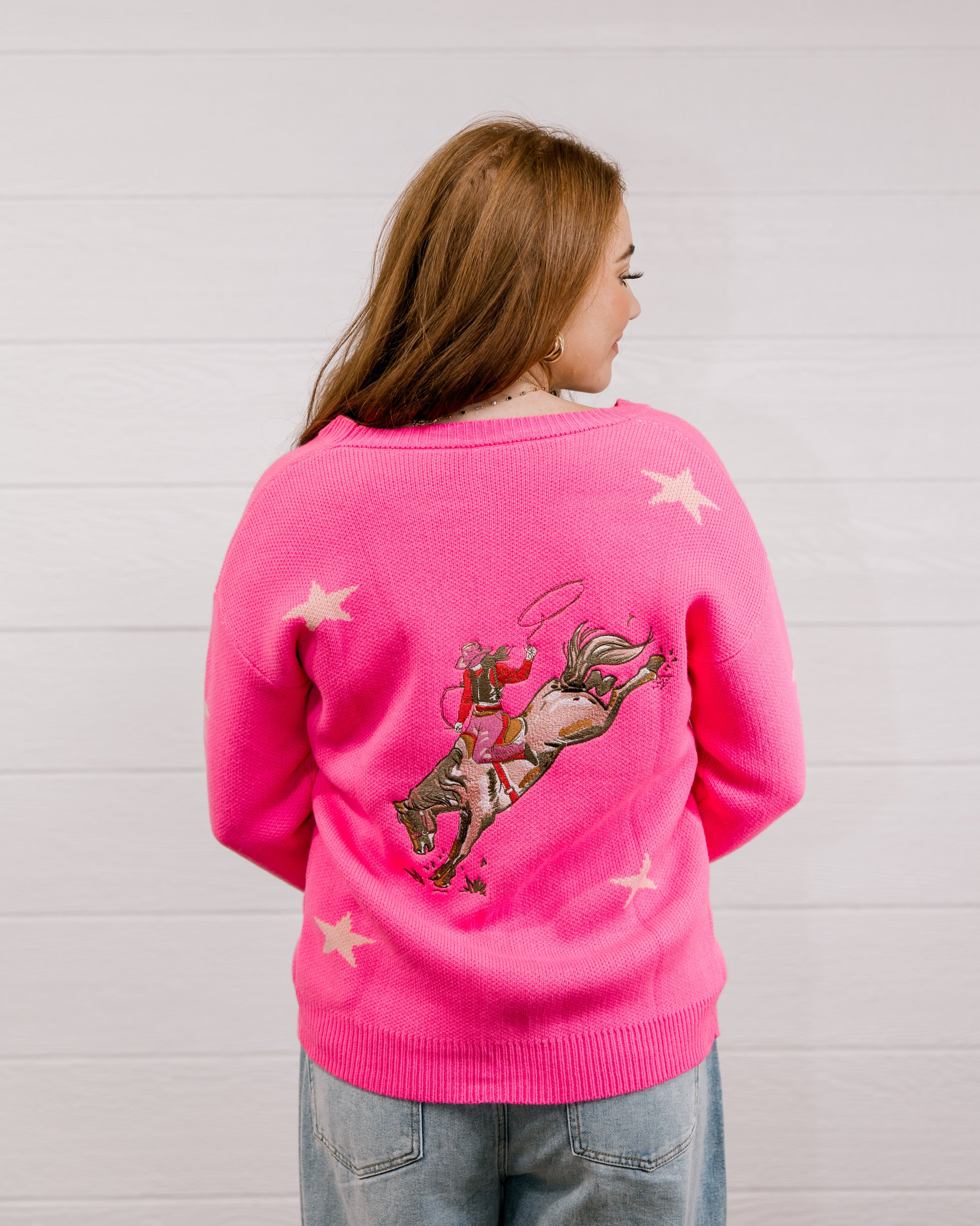 Back view of Woman wearing a bright pink cardigan with star patterns against a white background